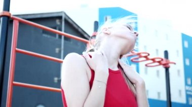 Genç, sarışın, iri göğüslü, at kuyruklu, kırmızı saçlı kadın spor sahasında boynunu uzatıyor.