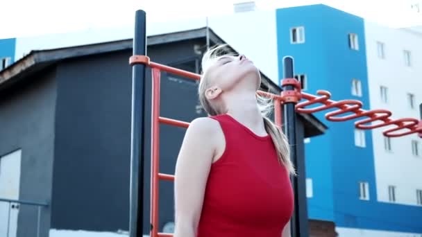 Mladá blondýnka busty žena s culíkem v červené horní natahuje krk na sportovním hřišti — Stock video