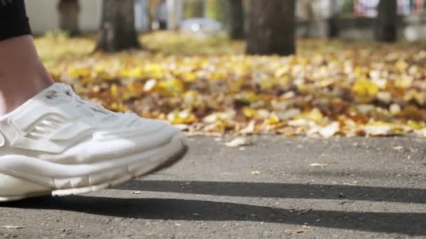 Primer plano de las piernas de las mujeres jóvenes en zapatillas blancas y leggings negros en el parque — Vídeos de Stock