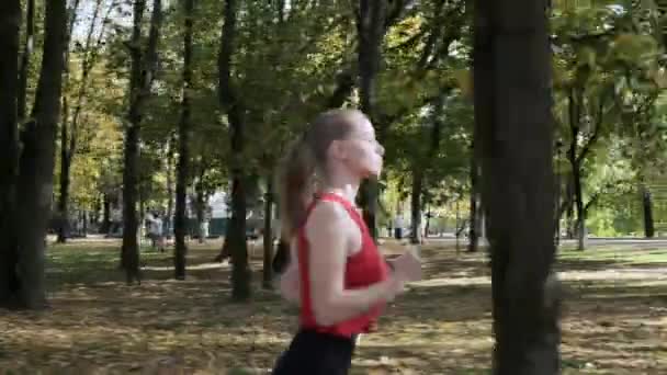 Gadis kulit putih berlari dengan pakaian olahraga berlari di taman musim gugur pada hari yang cerah — Stok Video