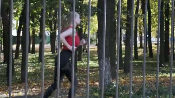白昼の秋の公園を走るスポーツウェア姿の白人フィットネスガールランナー — ストック動画