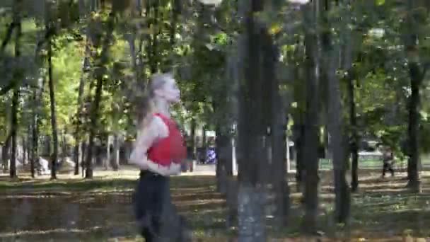 Kaukasische Fitness-Läuferin in Sportbekleidung läuft an sonnigem Tag im Herbstpark — Stockvideo