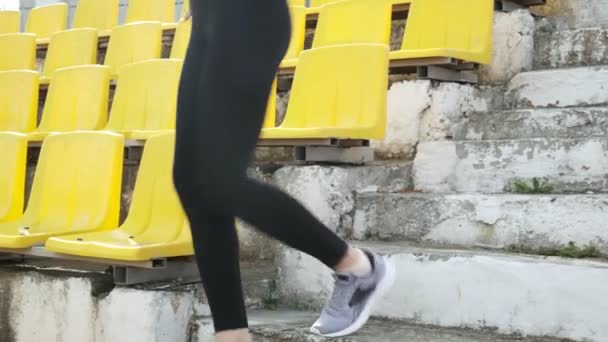 Spor giyimli sıska genç koşucu merdivenden iniyor, stadyum koltuğunda oturuyor. — Stok video