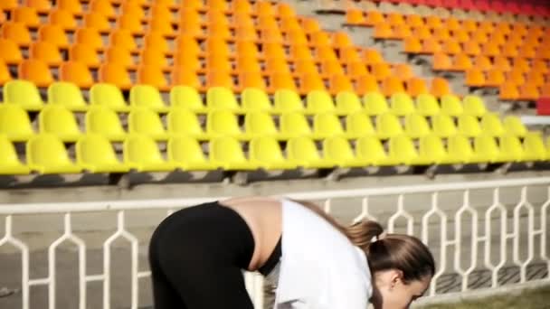 Młoda kobieta w sportowej odzieży rozciągającej ciało na tle stadionu sportowego — Wideo stockowe