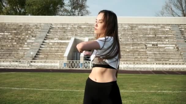 Young asian female in sportswear stretching arms at stadium field on sunny day — Stock Video