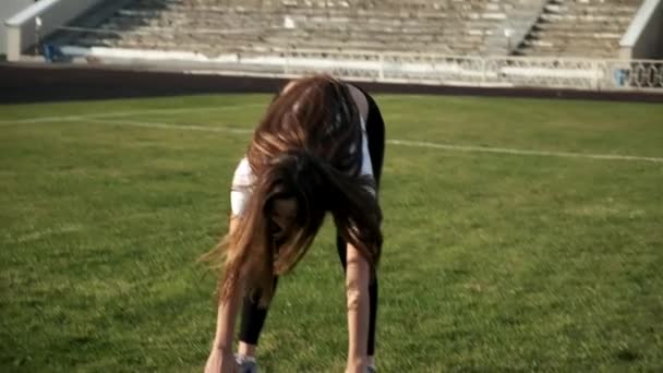 Jeune asiatique femelle dans sportswear étirement corps à stade champ sur sunny jour — Video