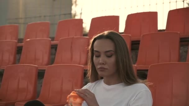 Sportovní hezká fena sedí na staduim tribune, pije vodu z plastové láhve — Stock video