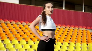Spor giyimli genç bir kadın spor stadyumunun arka planında esniyor.