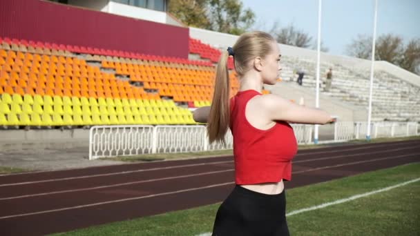 スポーツスタジアムを背景にスポーツウェアを着た若い女性が腕を伸ばし — ストック動画