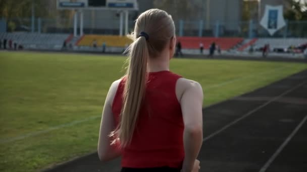 Последующий снимок молодого спортсмена в спортивной одежде, бегущего по стадионной дорожке — стоковое видео