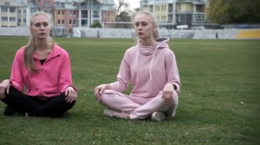 Pembe spor giyimli iki genç ikiz Lotus pozisyonunda çimlerde oturur, meditasyon yaparlar.