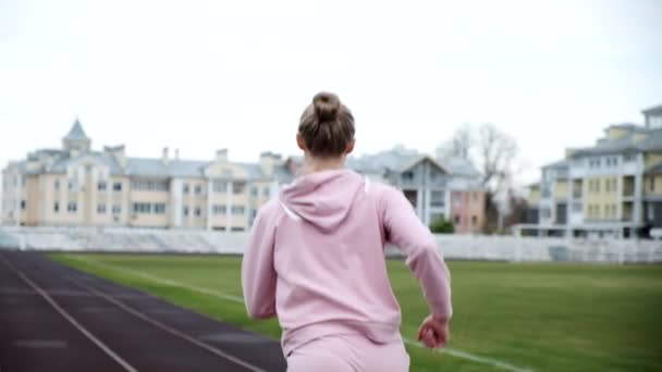 Acompanhamento do jovem corredor de fitness em sportswear correndo na pista do estádio — Vídeo de Stock