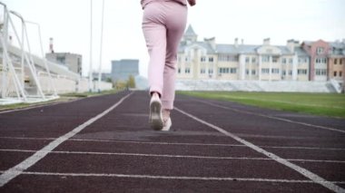 Pembe spor giyimli beyaz kadın koşucu stadyum pistinde koşuyor.