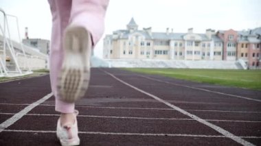Pembe spor giyimli beyaz kadın koşucu stadyum pistinde koşuyor.