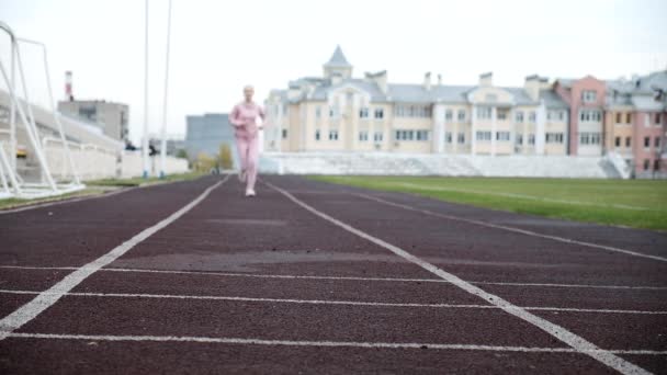 Passar kaukasiska ung kvinna löpare i rosa sportkläder som löper på stadion spår — Stockvideo