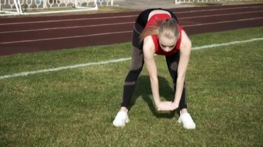 Spor giyimli genç bir kadın spor stadyumunun arka planında esniyor.