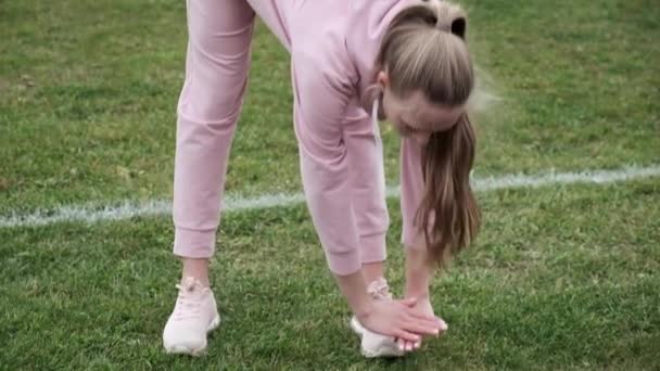 Młoda kobieta w sportowej odzieży rozciągającej ciało na stadionie sportowym boisko do piłki nożnej — Wideo stockowe