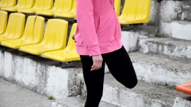 Spor kıyafetleri içinde genç beyaz kadın stadyum tribününde bacaklarını açıyor.