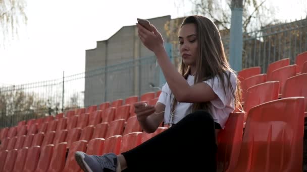 Ung passar asiatisk kvinna med hörlurar lyssnar på musik på smartphone på stadion — Stockvideo