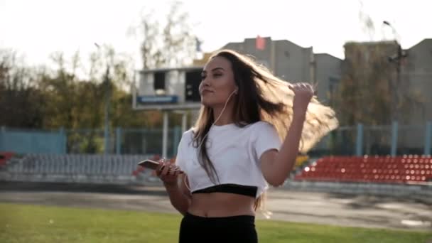 Wanita asia muda fit dengan headphone mendengarkan musik di smartphone di stadion — Stok Video