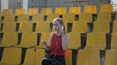 Kulaklıklı genç beyaz kadın stadyumda akıllı telefondan müzik dinliyor.