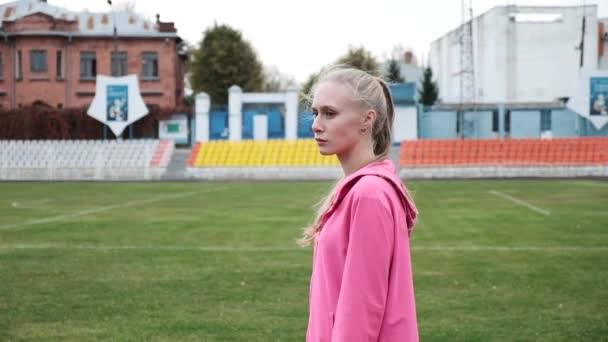 Fit girl en vêtements de sport se tient à l'extérieur au milieu du stade avant de remise en forme — Video