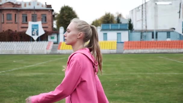 Ajuste caucásico bonita mujer en rosa ropa deportiva paseos a lo largo de hierba campo al aire libre — Vídeo de stock