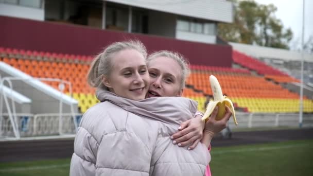 Dos hermanas gemelas idénticas en chaqueta rosa abrazándose y divirtiéndose en el estadio — Vídeo de stock