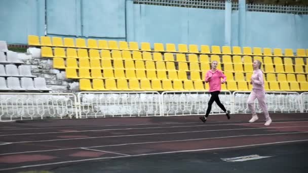 Dos hermanas gemelas idénticas caucásicas en ropa deportiva corriendo en pista de estadio — Vídeos de Stock