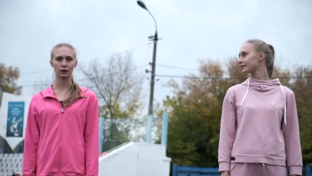 ピンクのスポーツウェアを着た同じ白人の双子の姉妹が屋外で一緒に走っています — ストック動画