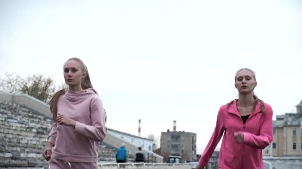 Idénticas hermanas gemelas caucásicas en ropa deportiva rosa corriendo juntas al aire libre — Vídeos de Stock