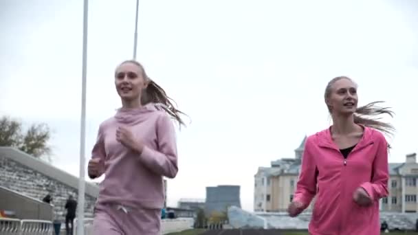 Identiska kaukasiska tvillingsystrar i rosa sportkläder som springer utomhus tillsammans — Stockvideo