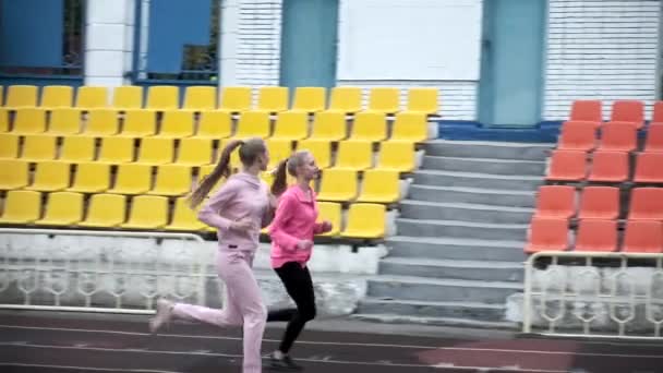 Duas irmãs gêmeas caucasianas idênticas em sportswear correndo na pista do estádio — Vídeo de Stock