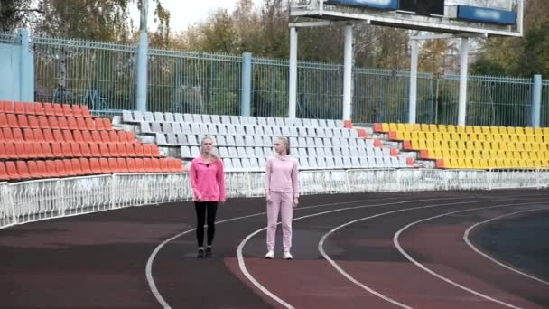 Duas irmãs gêmeas caucasianas idênticas em sportswear correndo na pista do estádio — Vídeo de Stock