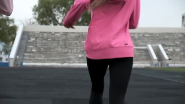 Vestire caucasico giovane corridore donne in rosa abbigliamento sportivo in esecuzione su pista stadio — Video Stock