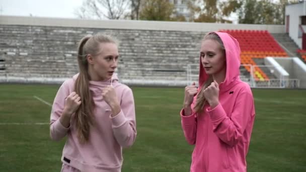 Young fit sporty caucasian pretty twin sisters boxing outdoors at stadium field — Stock Video