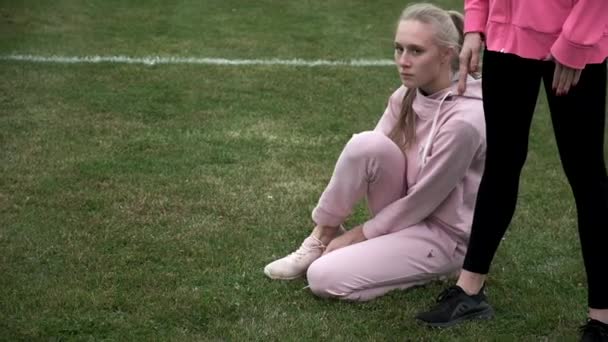 Idénticas hermanas gemelas en tren de ropa deportiva al aire libre, una de ellas ata cordones de zapatos — Vídeos de Stock