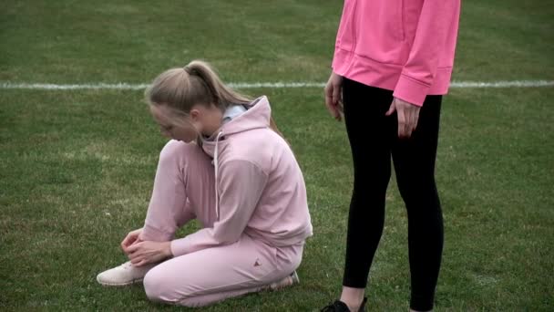 Idénticas hermanas gemelas en tren de ropa deportiva al aire libre, una de ellas ata cordones de zapatos — Vídeos de Stock