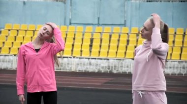 Spor giyimli beyaz ikizler stadyumda vücutlarını esnetiyorlar.