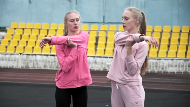 Unga kaukasiska identiska tvillingar i sportkläder sträcker sina kroppar på stadion — Stockvideo