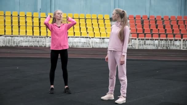Kaukasische identieke mooie tweeling in sportkleding doen squats oefening in het stadion — Stockvideo