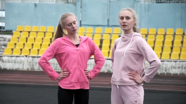 Due giovani gemelli caucasici in abbigliamento sportivo allungano i loro corpi allo stadio, si scaldano — Video Stock