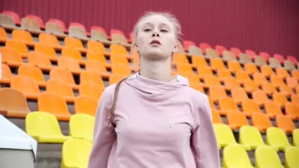 Νεαρή γυναίκα σε αθλητικά ρούχα τεντώνει τα όπλα στο παρασκήνιο του αθλητικού σταδίου — Αρχείο Βίντεο