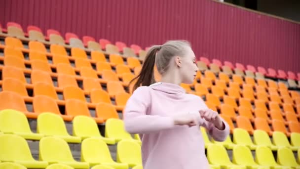 Młoda kobieta w odzieży sportowej rozciągająca ramiona na tle stadionu sportowego — Wideo stockowe