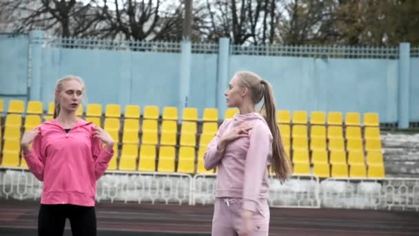 Unga kaukasiska identiska tvillingar i sportkläder sträcker sina kroppar på stadion — Stockvideo