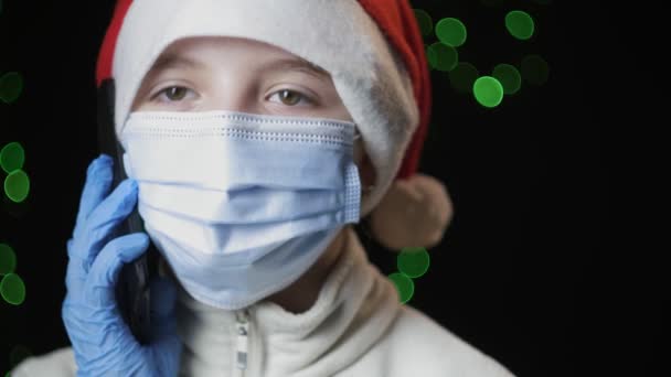 Meisje in de kerstman hoed, medisch beschermend masker, handschoenen spreekt op mobiele telefoon — Stockvideo