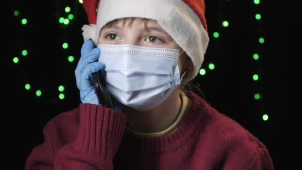 Meisje in rood kerstman hoed, blauw beschermend masker, handschoenen spreekt op mobiele telefoon — Stockvideo
