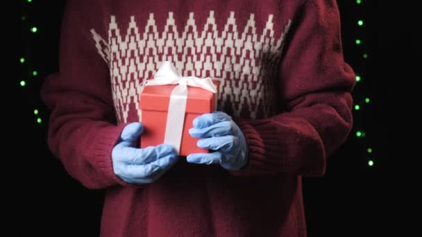 Primer plano en las manos en guantes protectores azules que sostienen la caja de regalo roja con cinta — Vídeo de stock