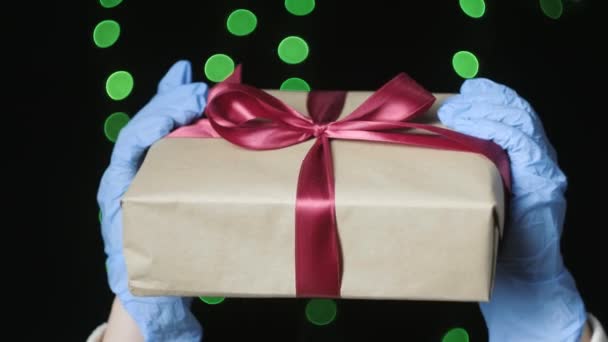 Manos de las personas en guantes protectores azules que sostienen la caja de regalo con cinta roja — Vídeos de Stock