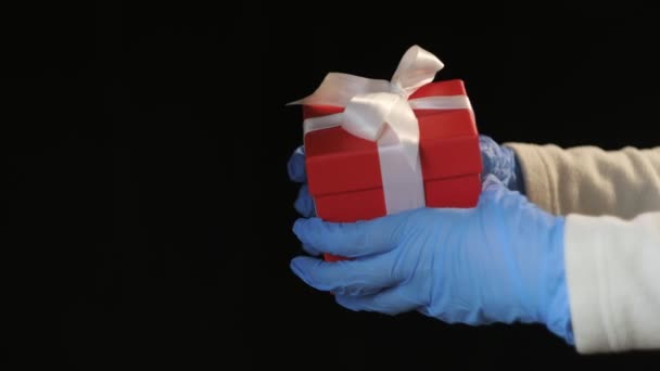 Manos de las personas en guantes protectores azules que sostienen la caja de regalo roja con cinta blanca — Vídeos de Stock